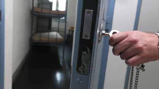 Eine Hand schließt eine Zellentür mit einem Schlüssel auf.