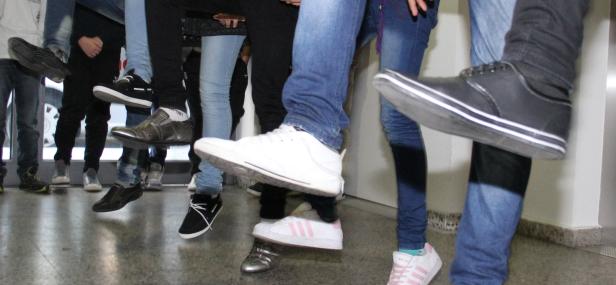 Mehrere Personen stehen mit verschiedenen Schuhen und Jeans auf einem Flur.