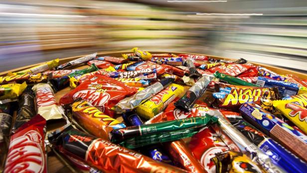 Eine Vielzahl von Süßigkeiten, darunter KitKat, Smarties und andere Schokoriegel, liegen auf einem Tisch.