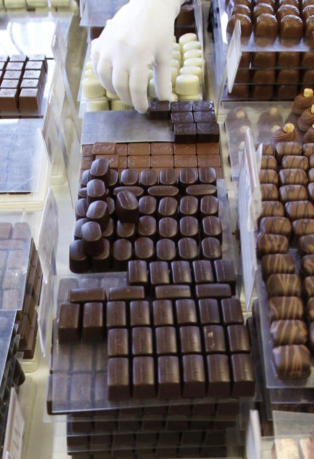 Eine Hand mit Handschuh ordnet Pralinen in einer Auslage an.