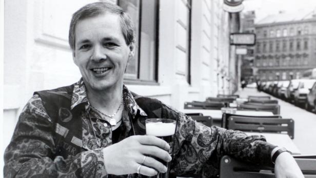 Ein Mann sitzt in einem Straßencafé und hält ein Glas dunkles Bier in der Hand.