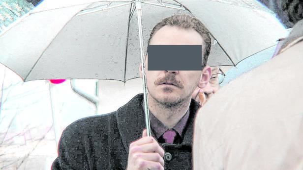 Ein Mann mit Schnurrbart hält einen Regenschirm im Regen.