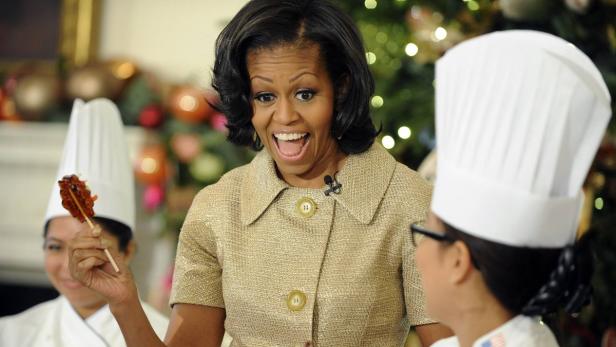 Michelle Obama betrachtet überrascht einen Kochlöffel mit Süßigkeiten.