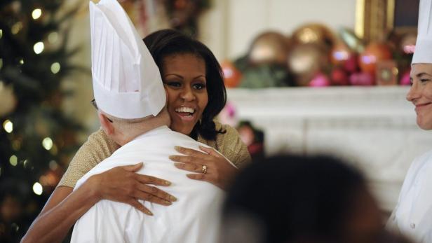 Michelle Obama umarmt einen Koch vor einem dekorierten Kamin.