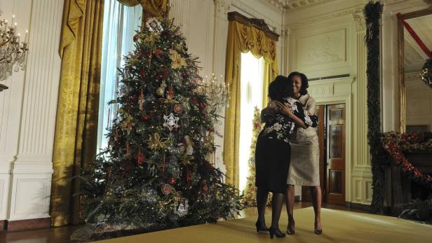 Michelle Obama umarmt eine Frau vor einem geschmückten Weihnachtsbaum im Weißen Haus.