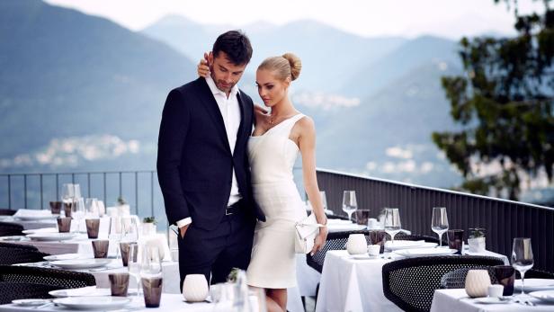 Ein Paar in eleganter Kleidung vor einem gedeckten Tisch mit Bergblick.