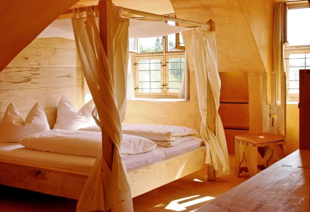 Ein Himmelbett mit weißen Vorhängen in einem hellen, sonnigen Zimmer.