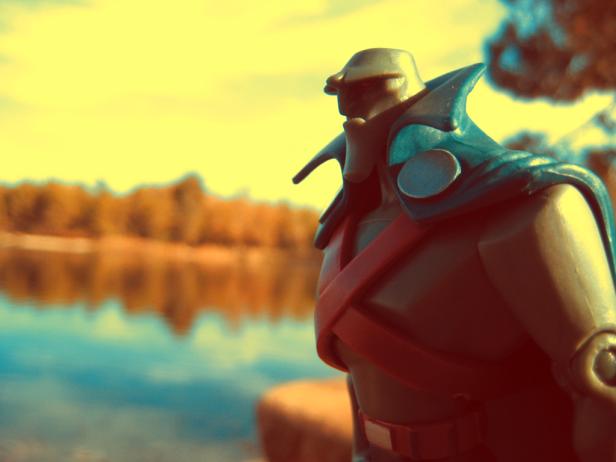 Eine Actionfigur mit Umhang steht vor einem See.