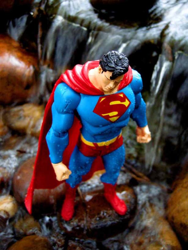 Eine Superman-Actionfigur steht im Wasser vor einem kleinen Wasserfall.