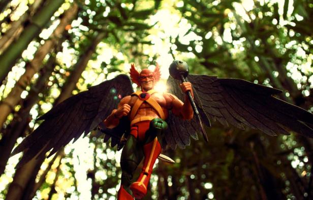 Eine Actionfigur von Hawkman mit Flügeln und einer Keule vor einem Waldhintergrund.