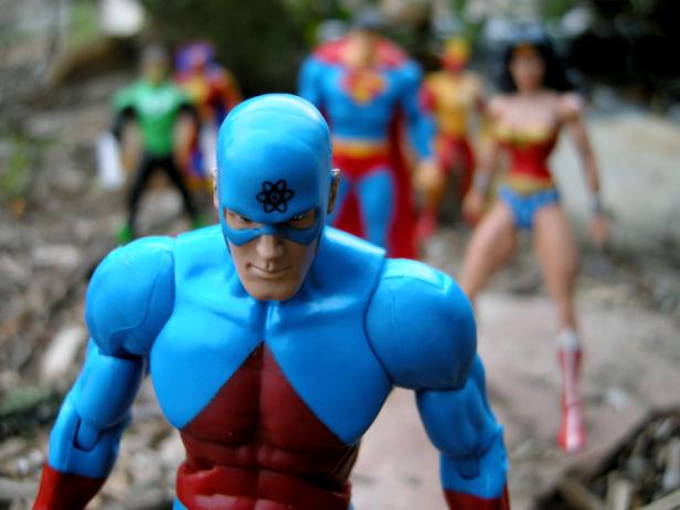 Actionfiguren von Atom, Wonder Woman, Superman und anderen Superhelden stehen im Freien.