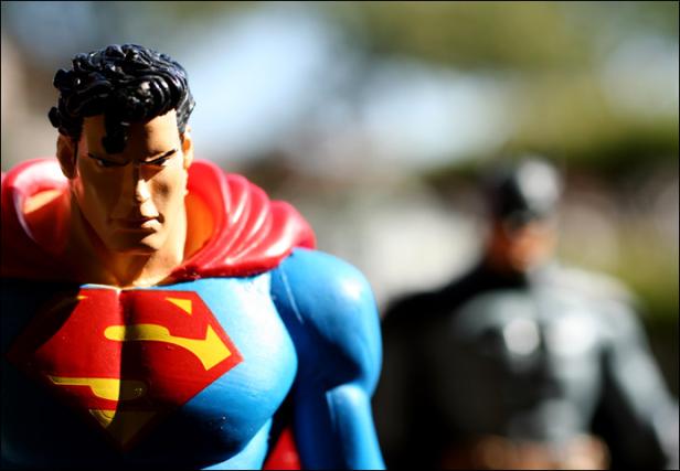 Eine Superman-Figur steht vor einer verschwommenen Batman-Figur.