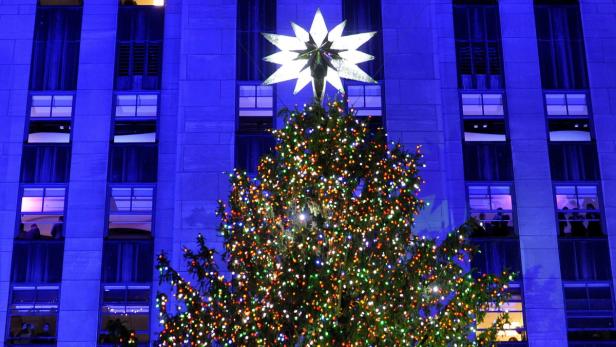 Ein Weihnachtsbaum mit bunten Lichtern und einem Stern vor einem Gebäude.