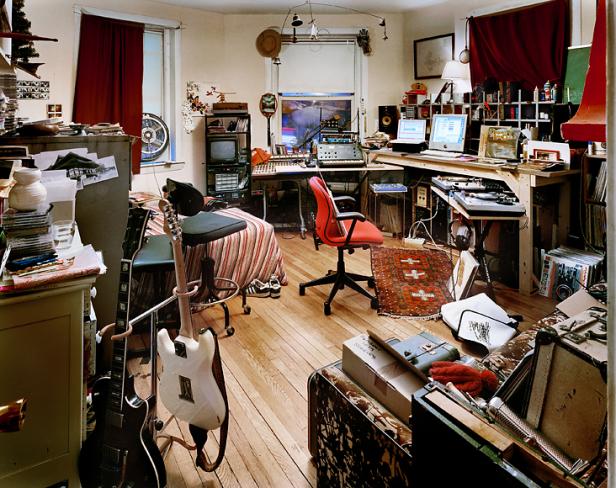 Ein chaotisches Zimmer mit Musikinstrumenten, Computern und Aufnahmegeräten.