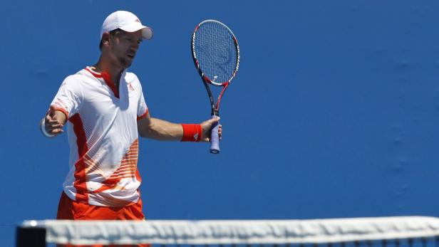 Ein Tennisspieler mit weißer Kappe und rotem Armband hält einen Tennisschläger.