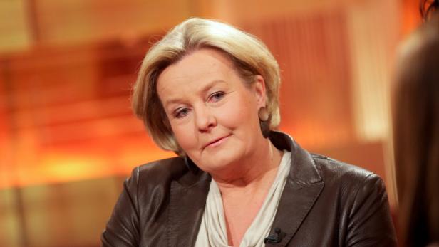 Eine Frau mit blonden Haaren und brauner Jacke schaut in die Kamera.