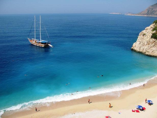 Ein Segelboot ankert vor einem Strand mit türkisfarbenem Wasser.
