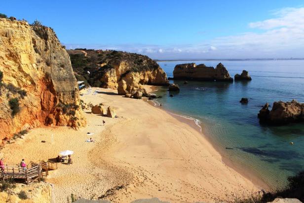 Blick auf einen Sandstrand mit Felsen und türkisfarbenem Wasser an der Algarve, Portugal.