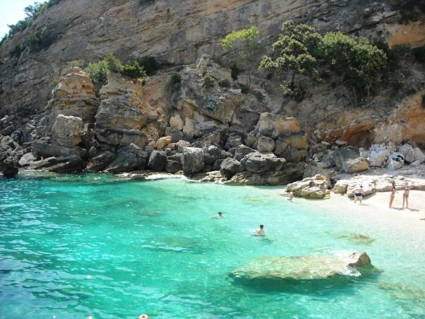 Menschen schwimmen und sonnen sich an einem Strand mit türkisfarbenem Wasser.