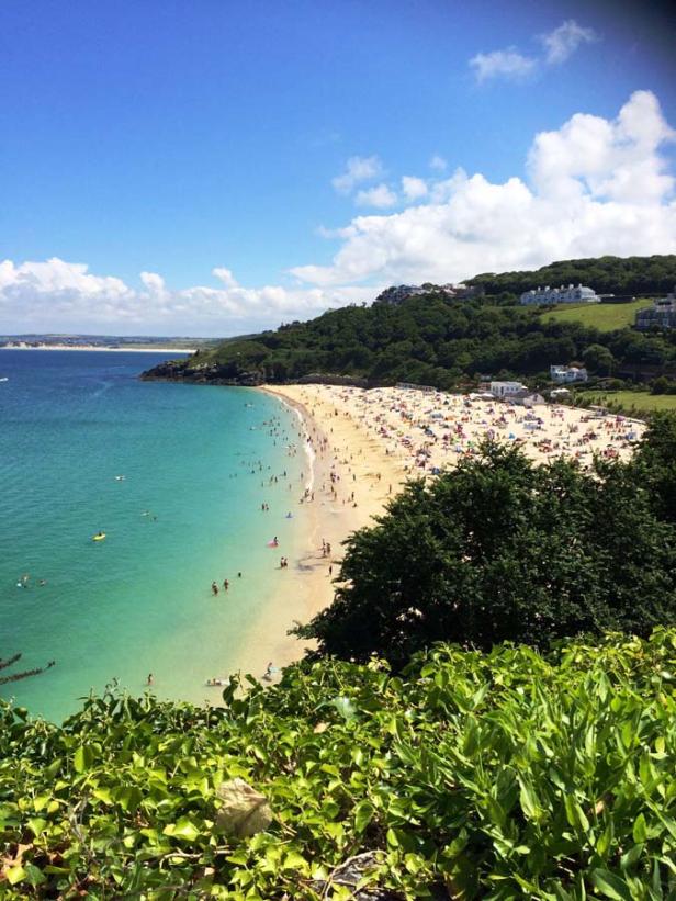 Ein voller Strand mit türkisfarbenem Wasser an einem sonnigen Tag.