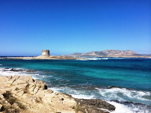 Ein alter Turm steht auf einer kleinen Insel vor einer bergigen Küste.