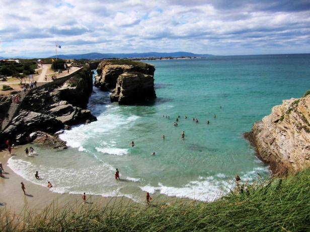 Blick auf einen Strand mit Felsformationen und Badegästen im türkisfarbenen Wasser.