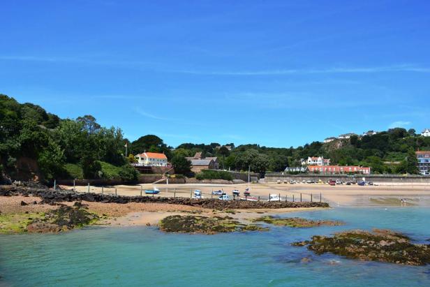 Blick auf eine Küstenlandschaft mit Sandstrand, Häusern und blauem Himmel.