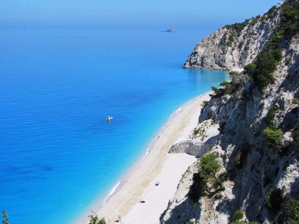 Ein langer Sandstrand erstreckt sich entlang einer felsigen Küste mit türkisfarbenem Wasser.