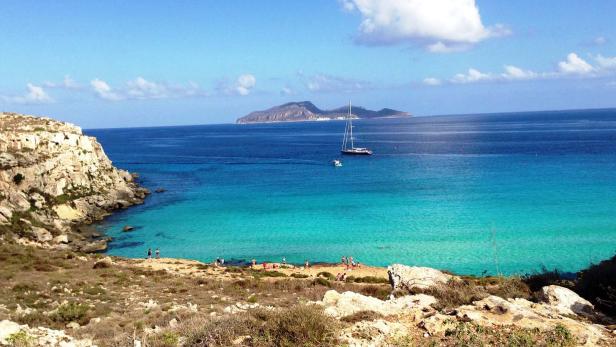 Eine malerische Küstenlandschaft mit türkisfarbenem Wasser, Klippen und einem Segelboot vor einer Insel.