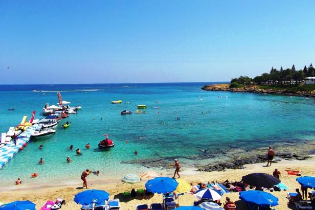 Ein sonniger Strand mit türkisfarbenem Wasser und vielen Badegästen.