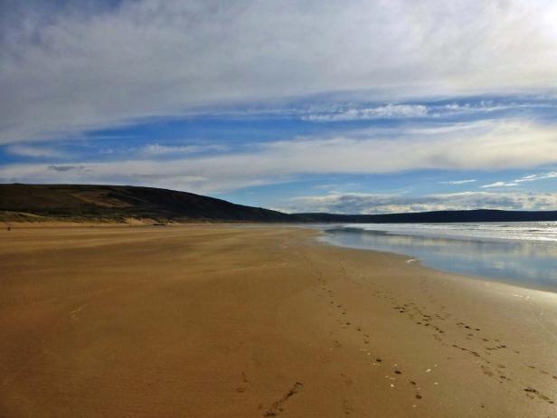 Ein weiter Sandstrand erstreckt sich unter einem bewölkten Himmel.