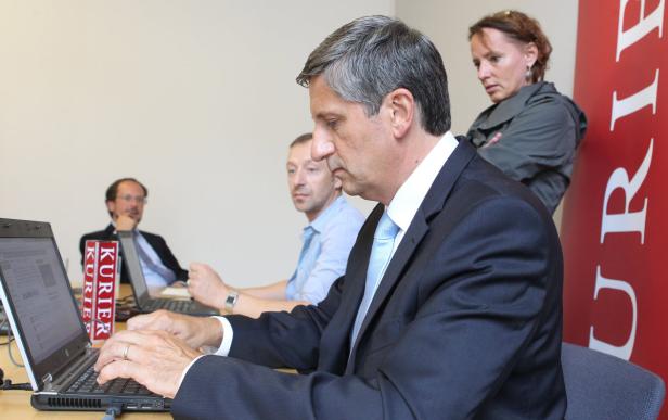 Ein Mann im Anzug tippt auf einem Laptop, während andere Personen im Hintergrund sitzen.