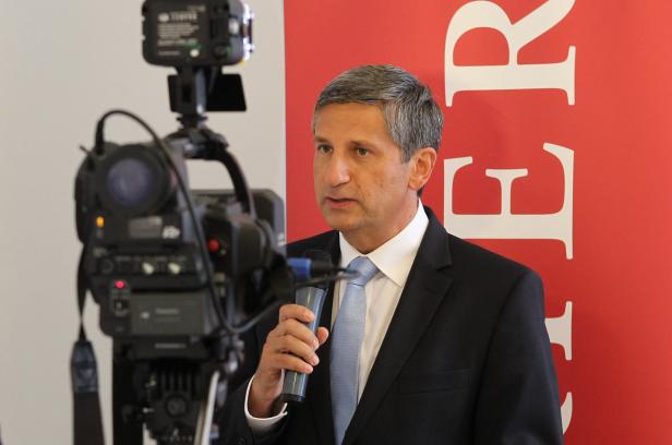 Ein Mann im Anzug spricht vor einer Videokamera in ein Mikrofon.