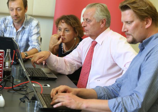 Eine Gruppe von Personen sitzt an einem Tisch und arbeitet an Laptops.