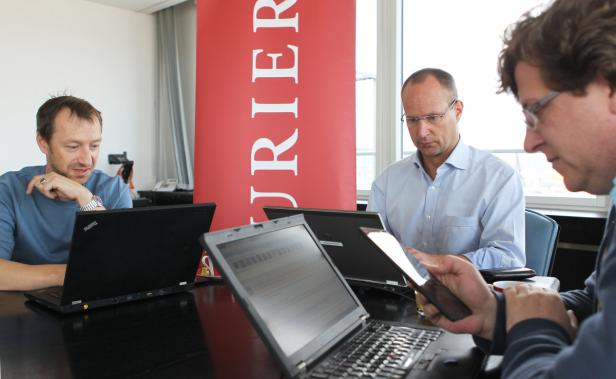 Drei Männer sitzen an einem Tisch mit Laptops und einem Tablet.