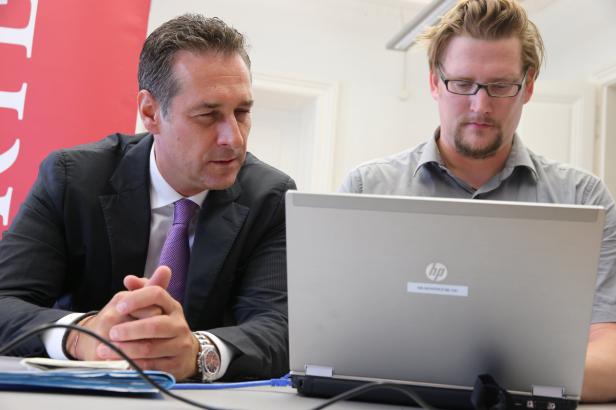 Zwei Männer sitzen an einem Tisch vor einem Laptop.
