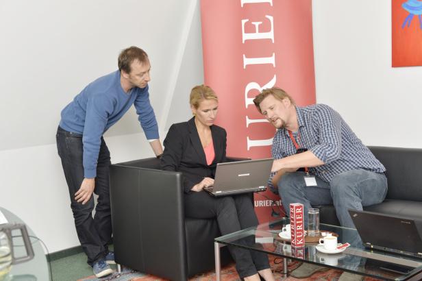Drei Personen sitzen und stehen um einen Tisch mit Laptops und diskutieren.