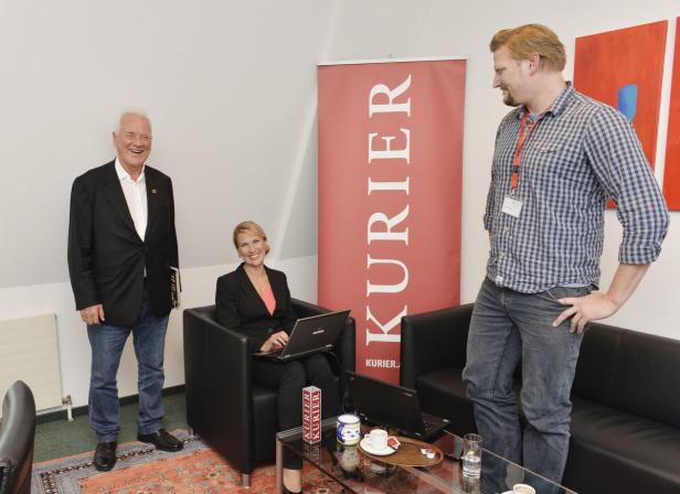 Drei Personen posieren vor einem Banner des „Kurier“.