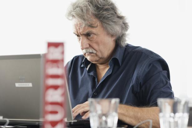 Ein Mann mit grauem Haar und Schnurrbart arbeitet konzentriert an einem Laptop.