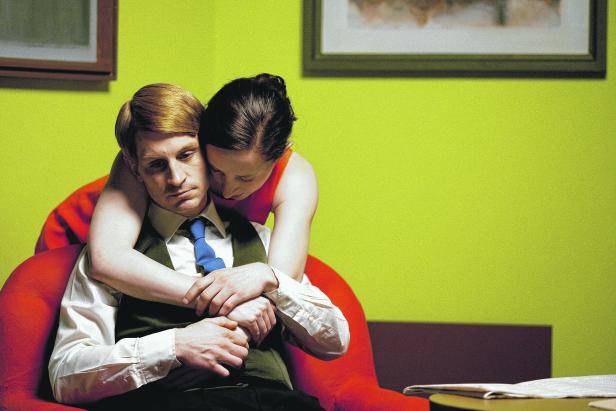 Eine Frau umarmt einen Mann, der in einem roten Sessel sitzt.