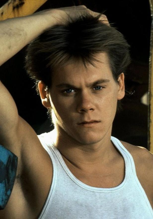 Ein junger Mann mit blau-grauen Augen und weißem Tanktop posiert selbstbewusst.