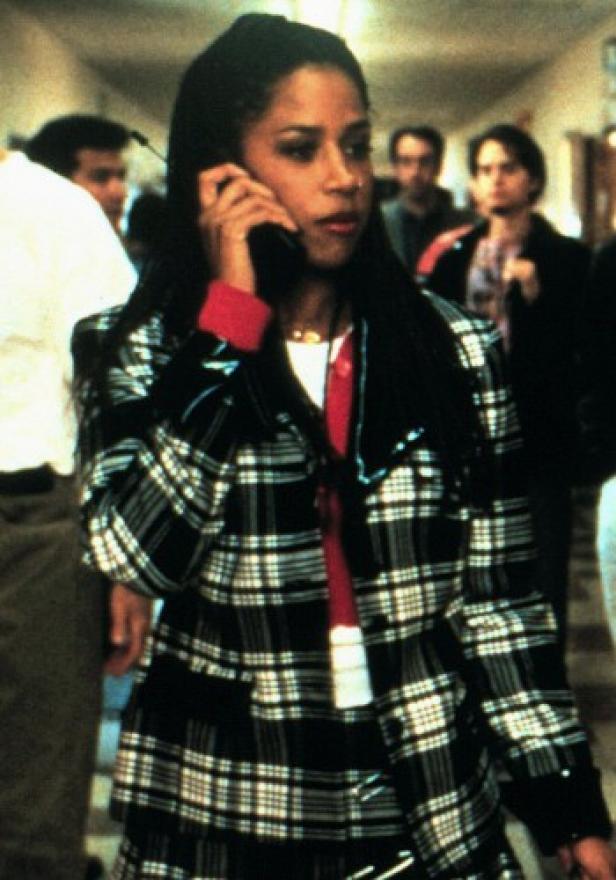 Eine Frau telefoniert in einem karierten Blazer in einem belebten Flur.