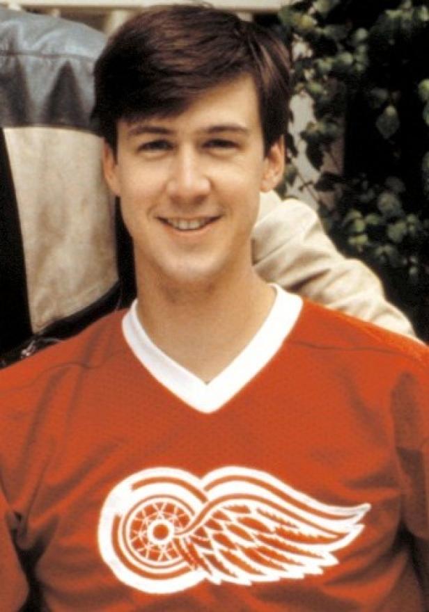 Ein lächelnder Mann trägt ein rotes Detroit Red Wings Trikot.