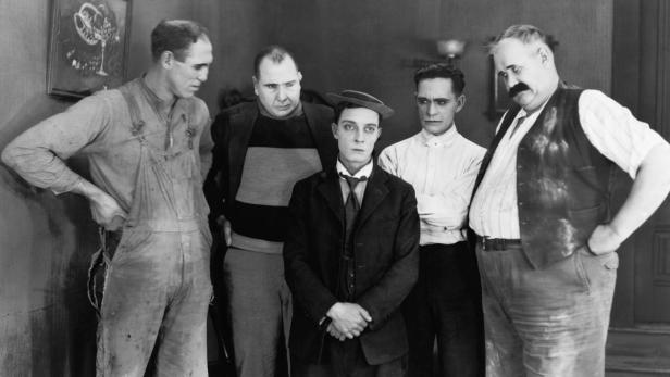 Buster Keaton steht mit vier weiteren Männern in einem Raum.