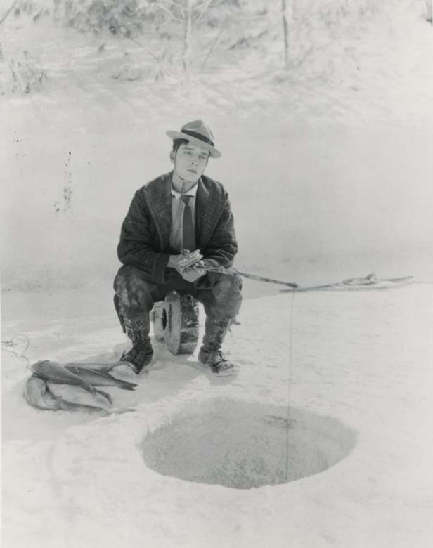 Ein Mann sitzt beim Eisangeln mit gefangenem Fisch neben einem Eisloch.