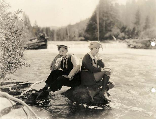 Buster Keaton und eine Frau sitzen in „The Balloonatic“ auf einem Felsen in einem Fluss.