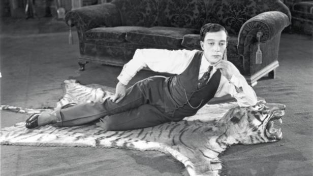 Buster Keaton liegt auf einem Tigerfell vor einem Sofa.