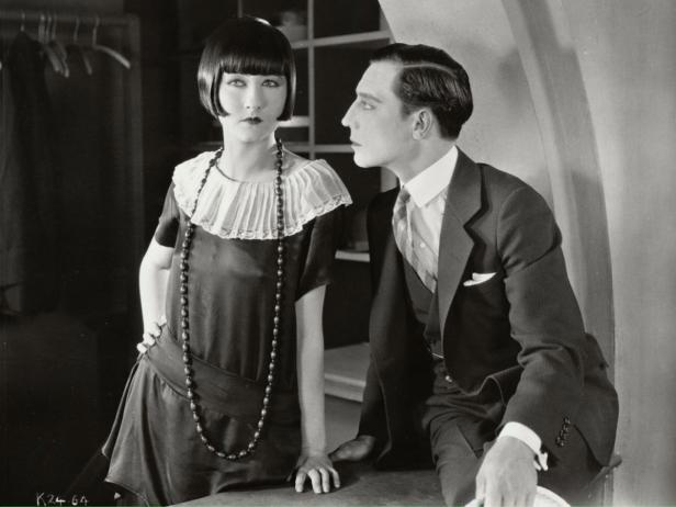 Eine Frau im Charleston-Kleid und ein Mann im Anzug posieren für ein Schwarzweißfoto.