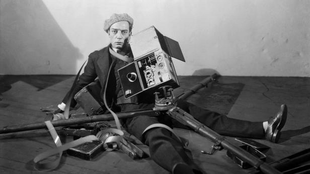 Ein Mann mit einer alten Filmkamera sitzt auf dem Boden.
