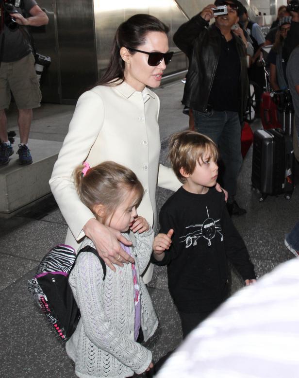 Angelina Jolie mit ihren Kindern an einem Flughafen, umgeben von Paparazzi.